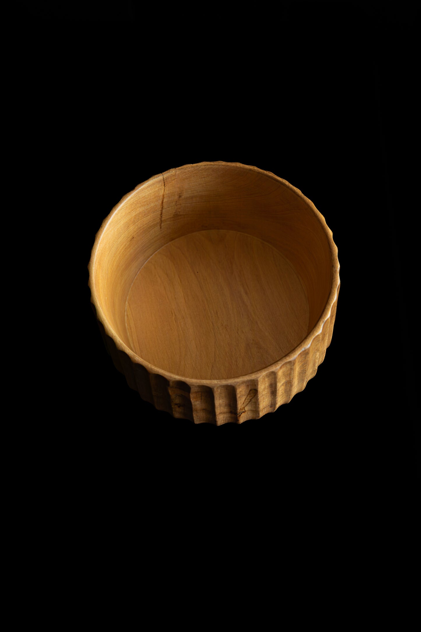Wooden cup with fluted design on a black background